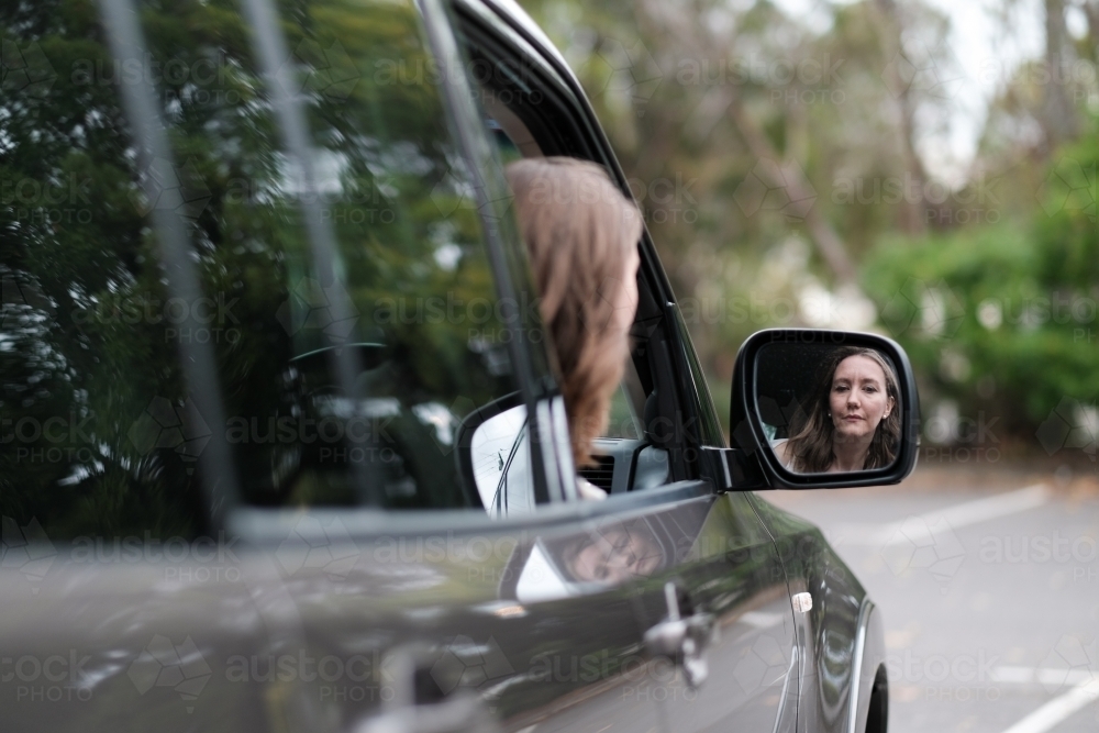 Young woman in 4wd vehicle looking in rear view mirror while parking - Australian Stock Image