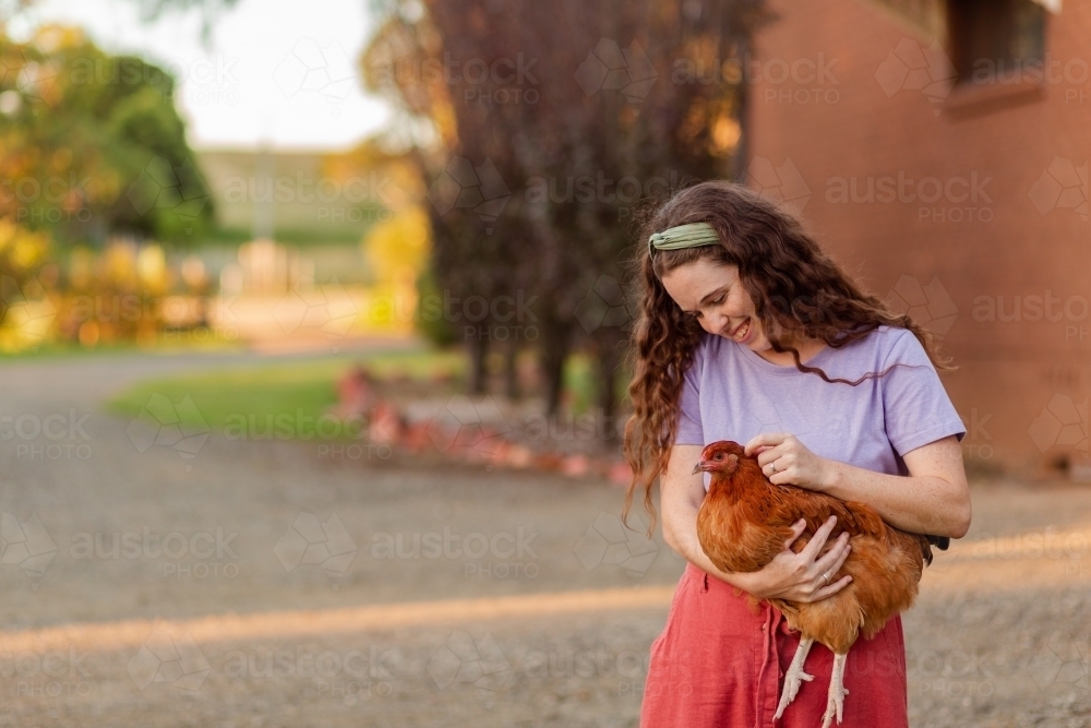 Young woman in country holding chook in arms with copy space - Australian Stock Image