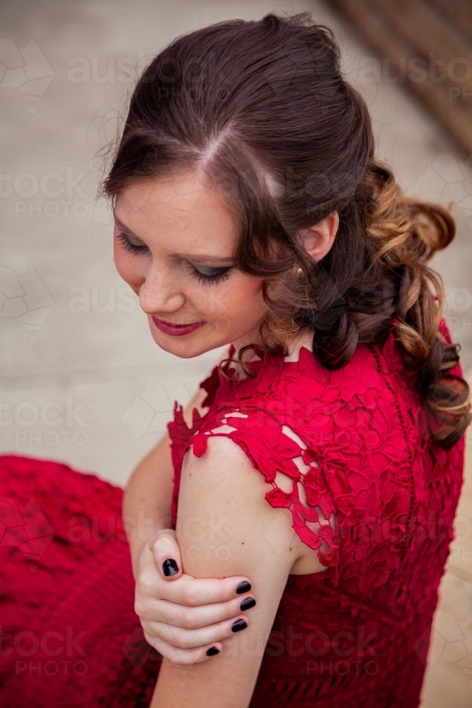 Young woman in red dress looking down hair and makeup done for school formal - Australian Stock Image