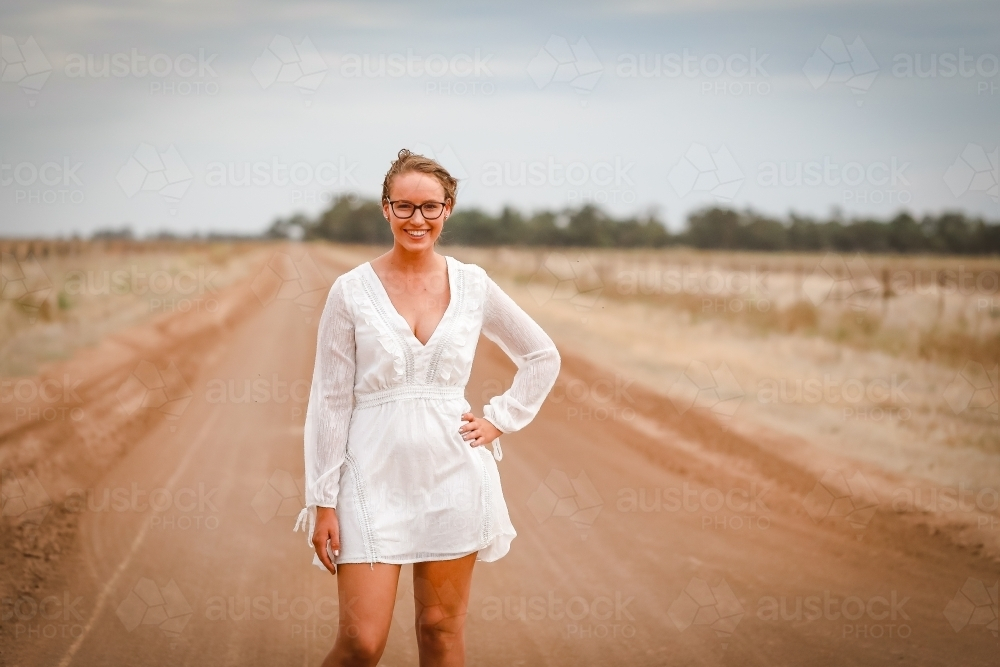 Young woman in white standing on rural dirt road - Australian Stock Image