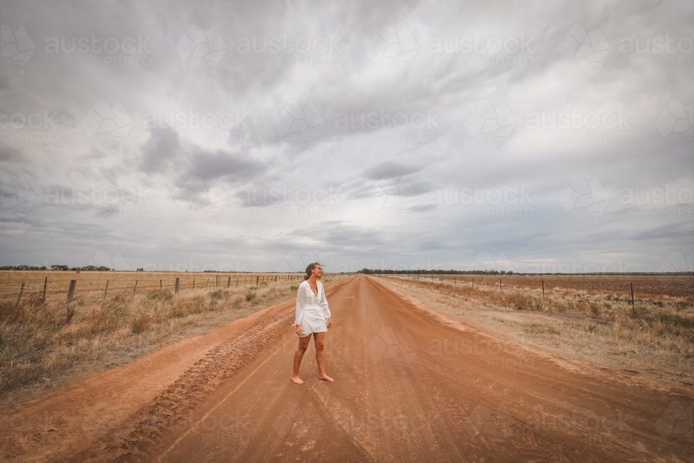 Young woman in white walking barefoot on rural dirt road - Australian Stock Image