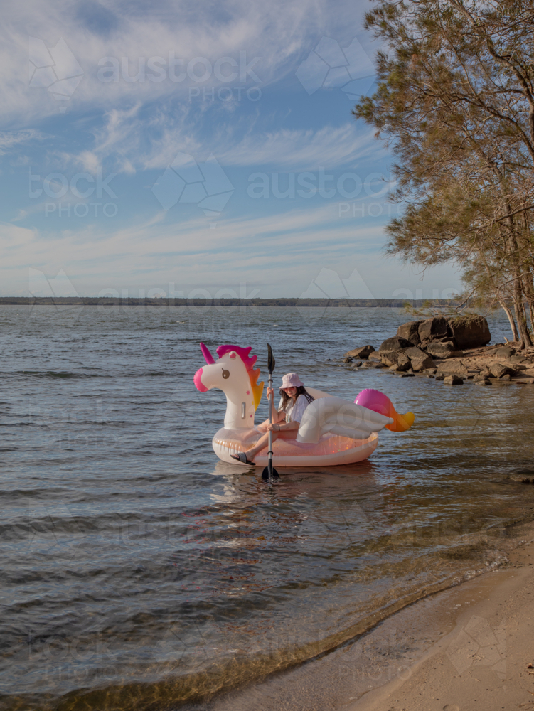 Young woman on a blow up unicorn on water - Australian Stock Image