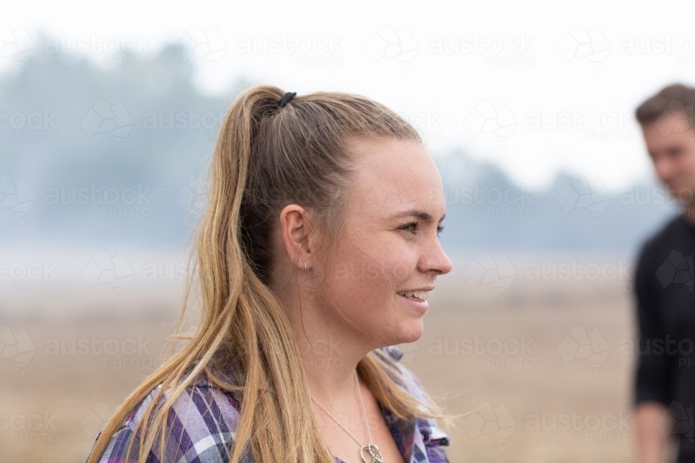 Young woman outdoors with man in background - Australian Stock Image