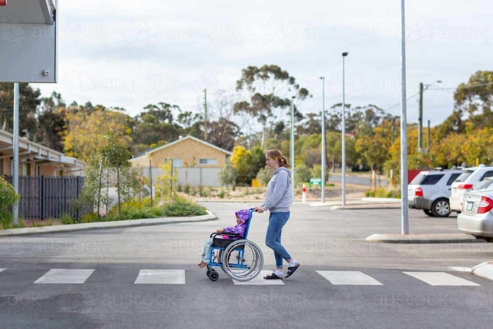 Young woman pushing small child in wheelchair - Australian Stock Image