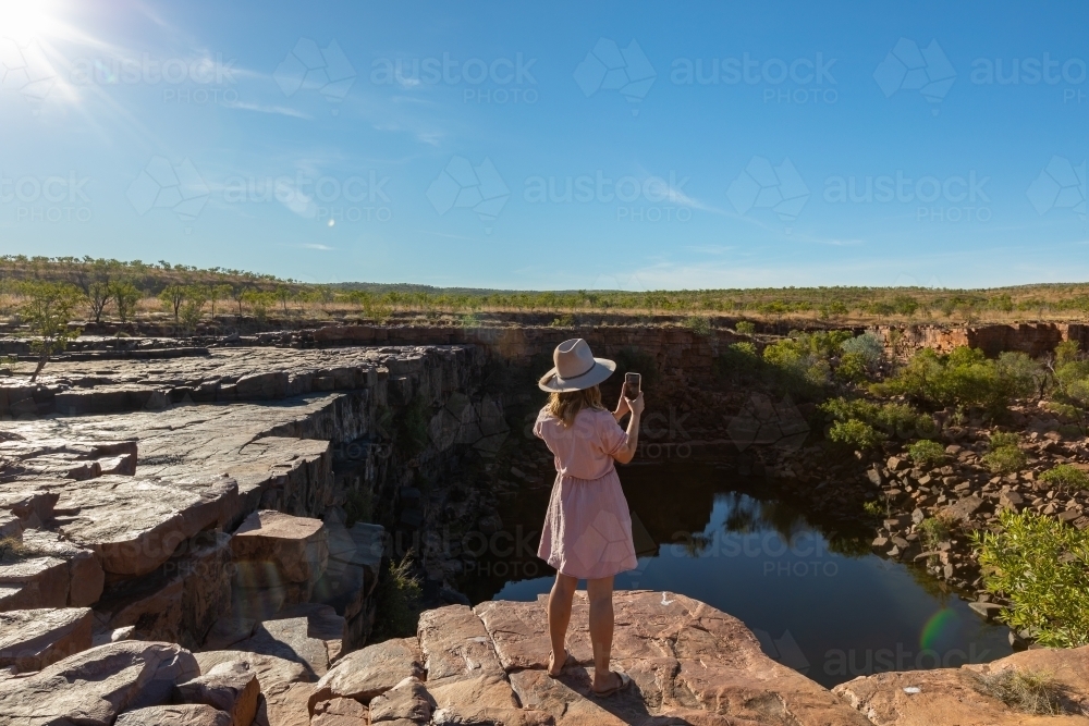 young woman seen from behind taking phone photo of landscape - Australian Stock Image