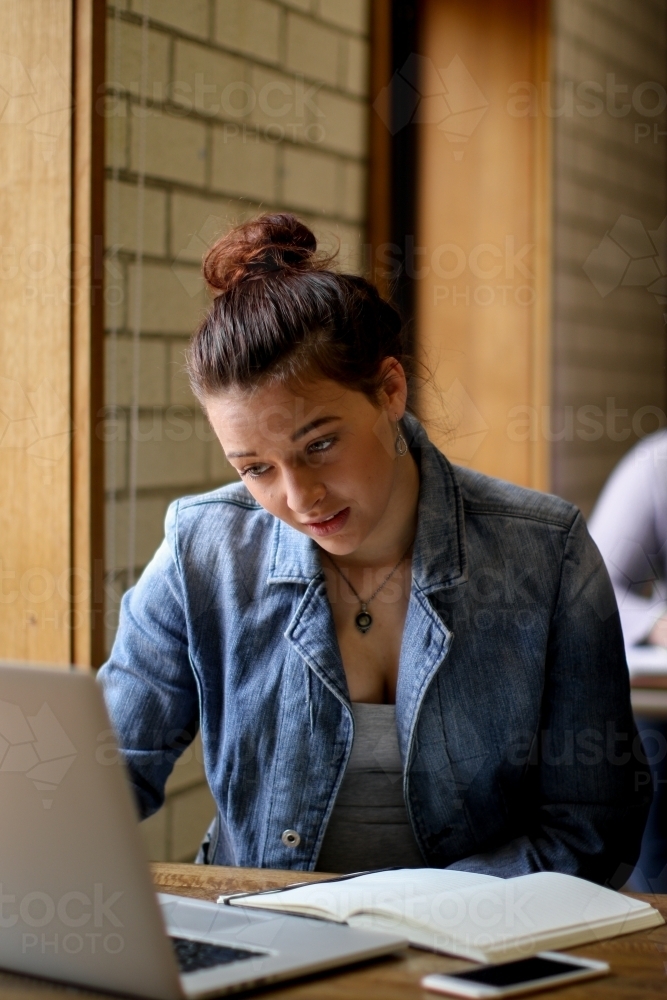 Young woman sitting at desk studying with books and laptop - Australian Stock Image