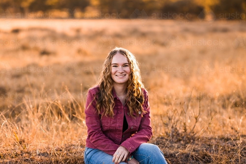 Young woman sitting in paddock on farm smiling - Australian Stock Image