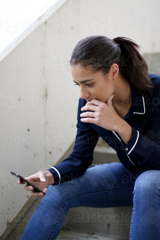 Young woman sitting in stairwell using mobile phone - Australian Stock Image