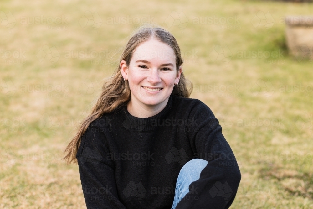 Young woman sitting on grass smiling - Australian Stock Image