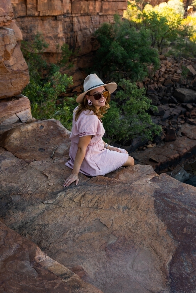 young woman sitting on rock ledge overlooking waterhole in the kimberley - Australian Stock Image