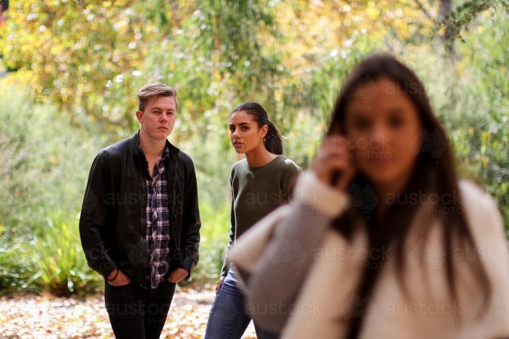 Young woman standing in front of a group of friends using a mobile phone - Australian Stock Image