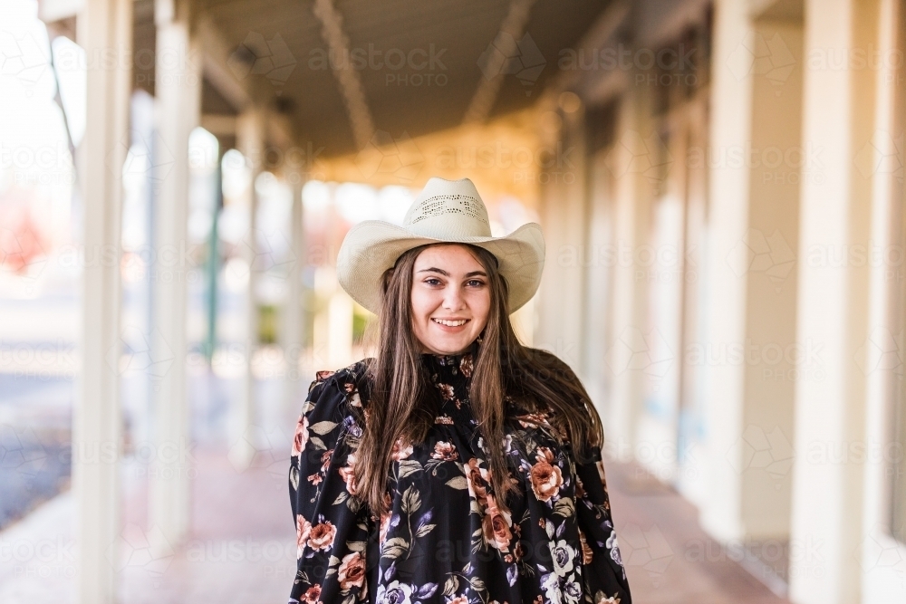 Young woman standing in main street wearing hat and floral shirt smiling - Australian Stock Image