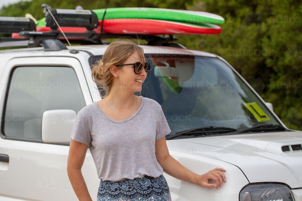 Young woman standing near vehicle with surfboards on roof - Australian Stock Image