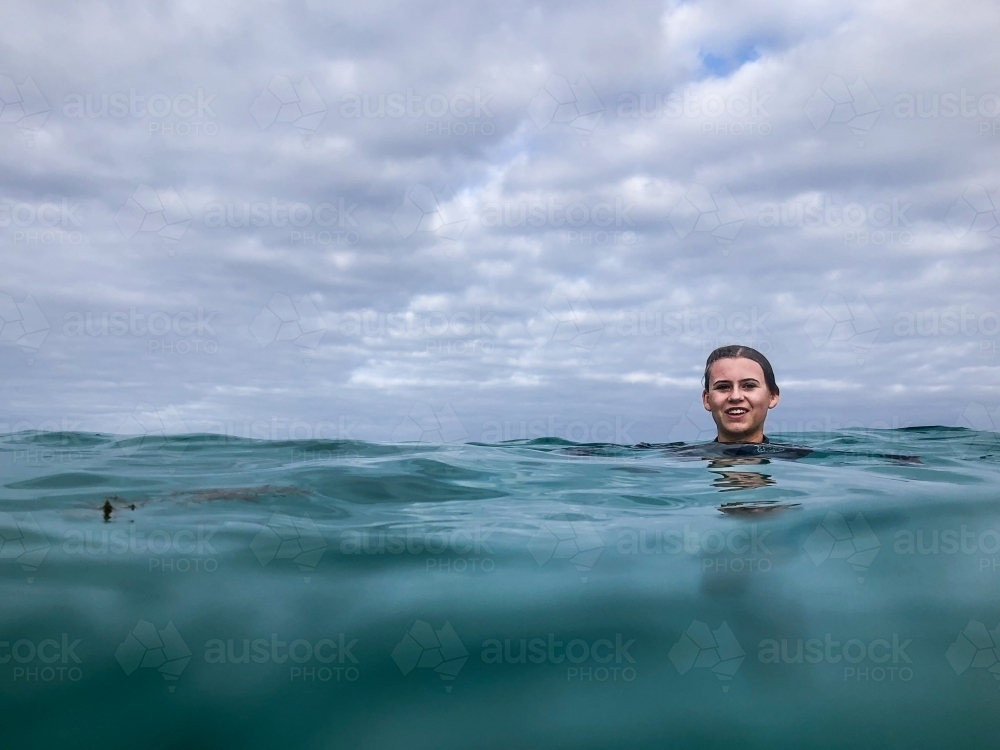 Young woman swimming in ocean on overcast day - Australian Stock Image