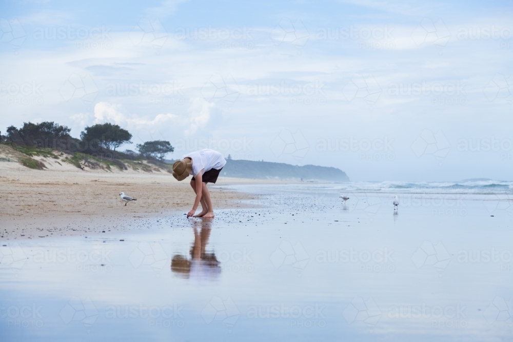 Young woman walking along beachcombing looking for shells at the seaside - Australian Stock Image