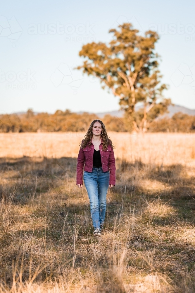 Young woman walking through long grass in paddock - Australian Stock Image