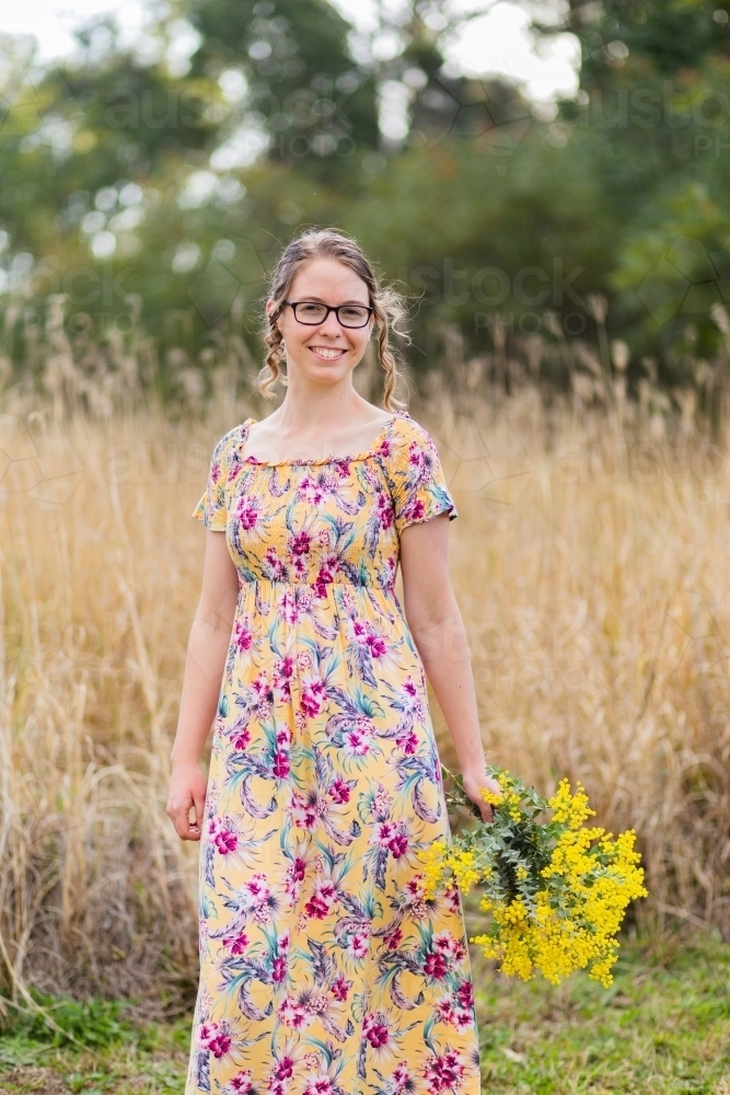 Young woman with bouquet of wattle blossoms outside in nature - Australian Stock Image