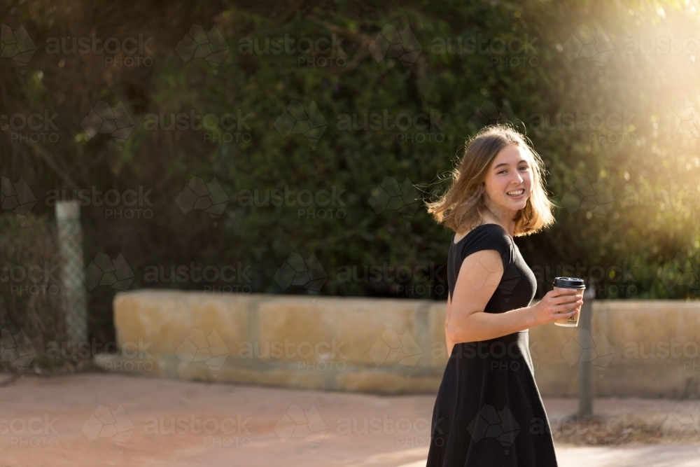 Young woman with coffee walking away looking over shoulder - Australian Stock Image