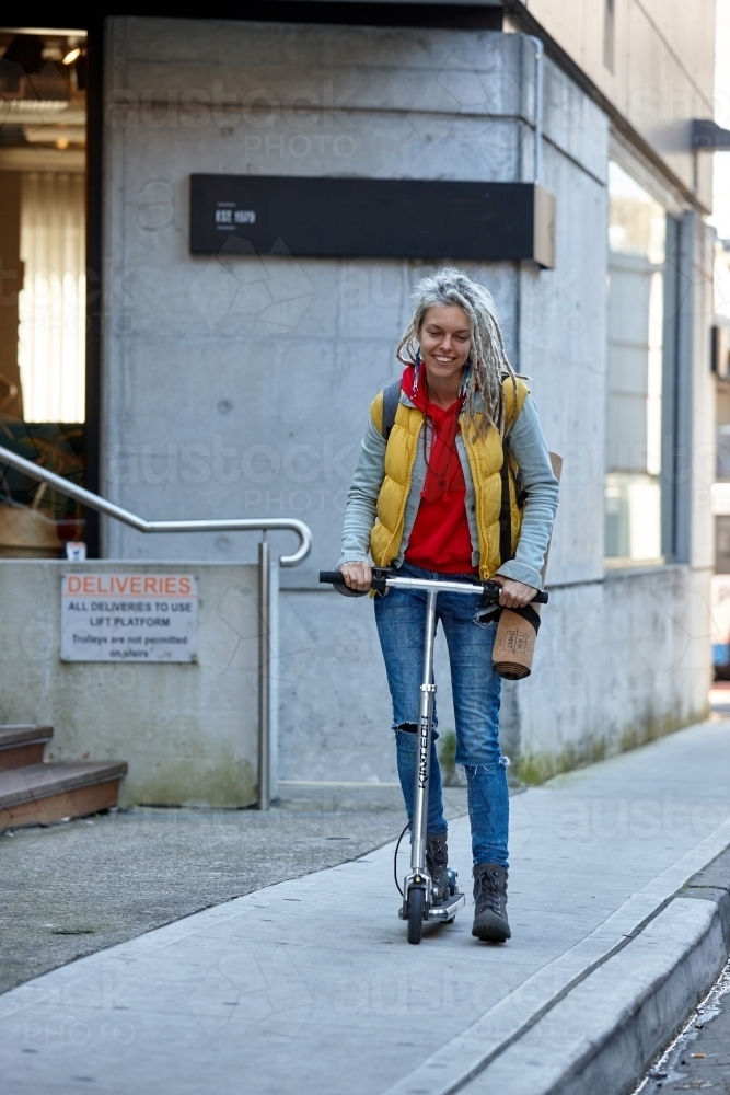 Young woman with dreadlocks riding electric scooter - Australian Stock Image