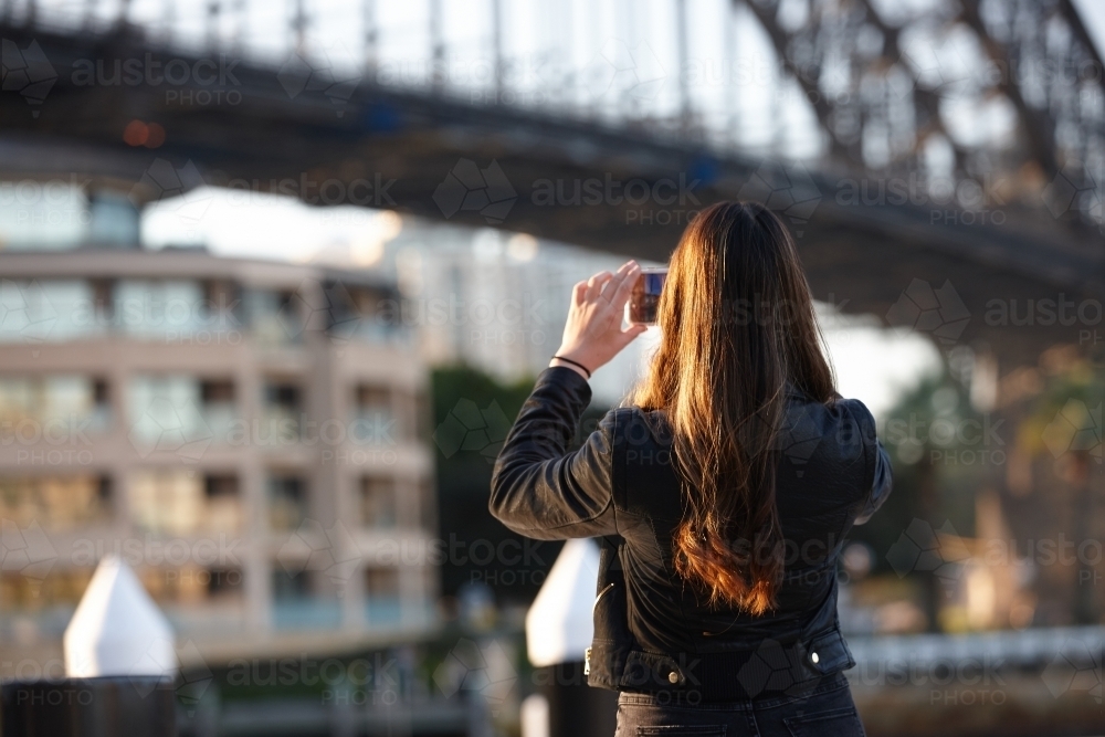 Young woman with mobile phone in front of harbour bridge - Australian Stock Image