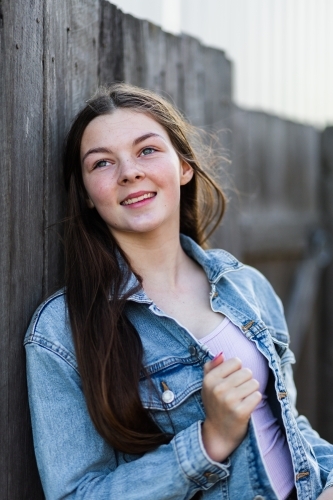 14yo girl leaning on fence looking up dreamily - Australian Stock Image