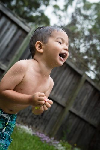 3 year old mixed race boy plays excitedly with water bombs in suburban backyard - Australian Stock Image