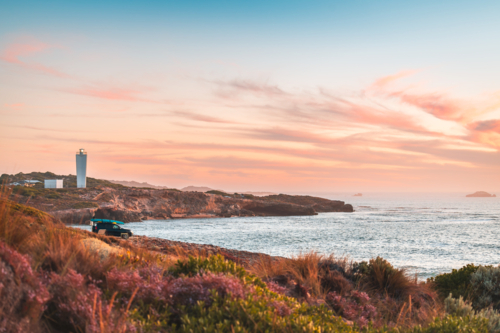 4WD car parked on rocky beach in Robe with driver enjoying the scenic sunset view with ocean - Australian Stock Image