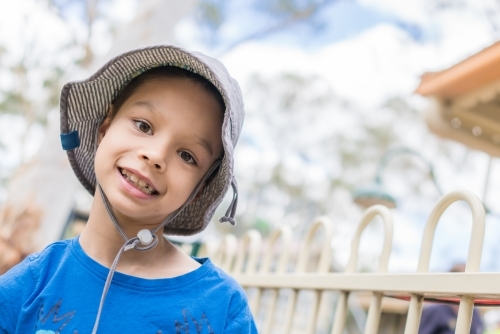 7 year old mixed race boy smiling and wearing a hat outside - Australian Stock Image