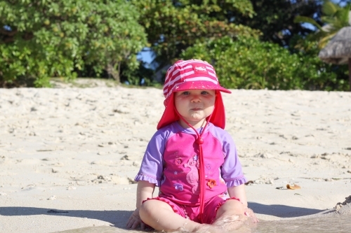 A 10 month old baby girl sitting on the sand in the shallow water at a beach in Australia - Australian Stock Image