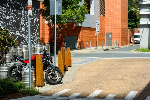 A back street intersection in Brisbane with motorbike, beer kegs, street signs and woman walking in - Australian Stock Image