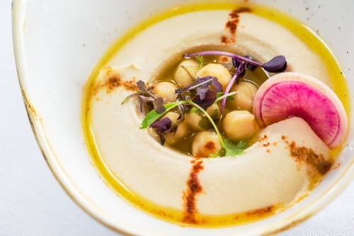 A bowl of hummus topped with chickpeas, herbs, and olive oil. - Australian Stock Image