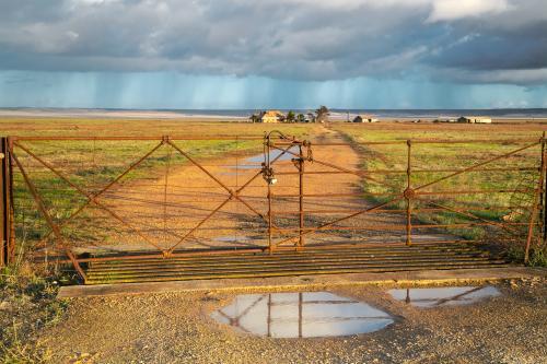 A closed gate on a farm in sunlight with rain and clouds overhead