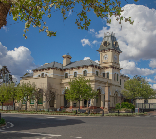 A country town post office framed by green leaves underneath a cloudy blue sky - Australian Stock Image