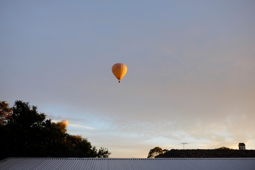 A couple of yellow hot air balloons floating above the suburbs - Australian Stock Image