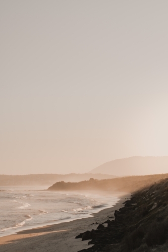 A deserted beach and headland during a hazy sunset.