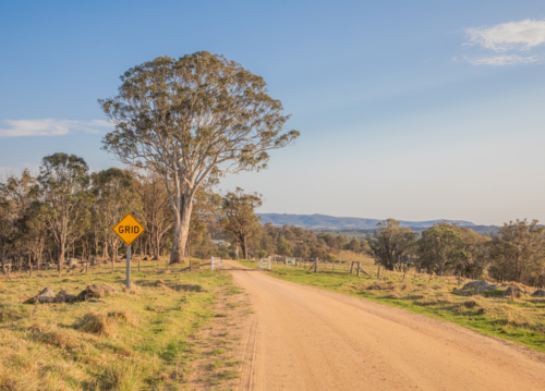 A dirt country road and a cattle grid crossing under a blue sky - Australian Stock Image