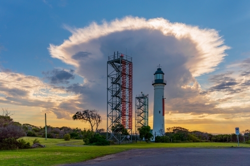 A dramatic storm cloud above a lighthouse and signal towers at sunrise at sunrise
