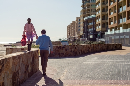 a father holding his daughter's hand as she walks along a high wall - Australian Stock Image