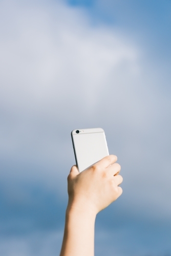 A female holding mobile phone against blue sky background. - Australian Stock Image