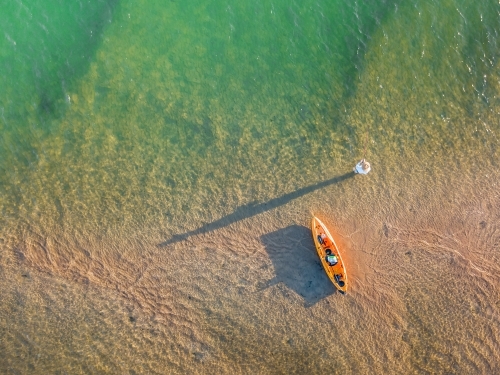 A fishermen alongside a kayak casting long shadows over a river