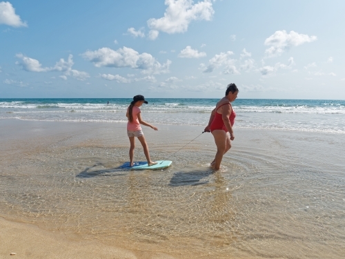 A grandmother pulling a girl on a surf board along an empty beach - Australian Stock Image