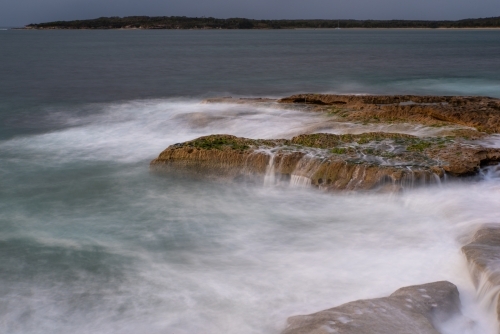 A grey dawn with waves breaking over rocks - Australian Stock Image