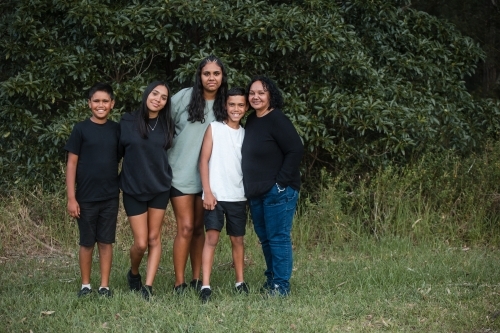 A happy Aboriginal family standing in field for a family portrait - Australian Stock Image