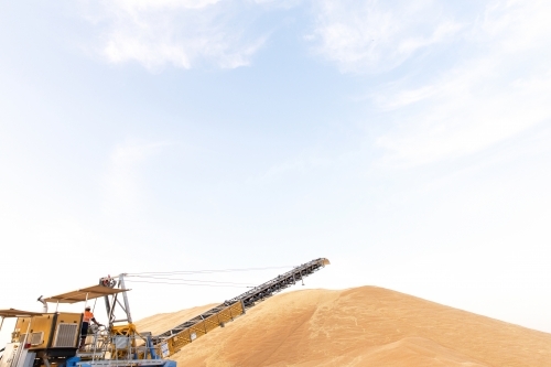 A hill of sand and yellow crane with one male operator standing on it - Australian Stock Image