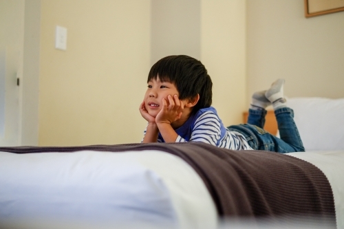 a kid lying on a bed watching tv