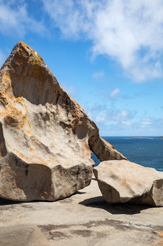 A large rock formation and a boulder under a cloudy blue sky - Australian Stock Image