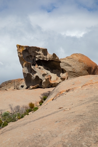 A large rock formation in sunlight full of holes and crevices with cloud above - Australian Stock Image