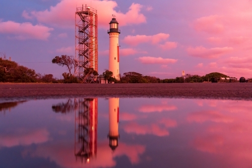 A lighthouse and its reflection against a colourful sunset sky - Australian Stock Image