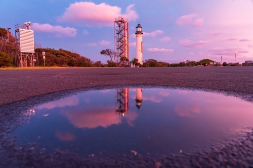 A lighthouse and signal tower at sunset reflected in a puddle - Australian Stock Image