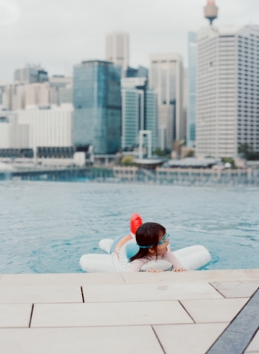 A little toddler girl swimming on a rooftop featuring the Sydney skyline in the background - Australian Stock Image